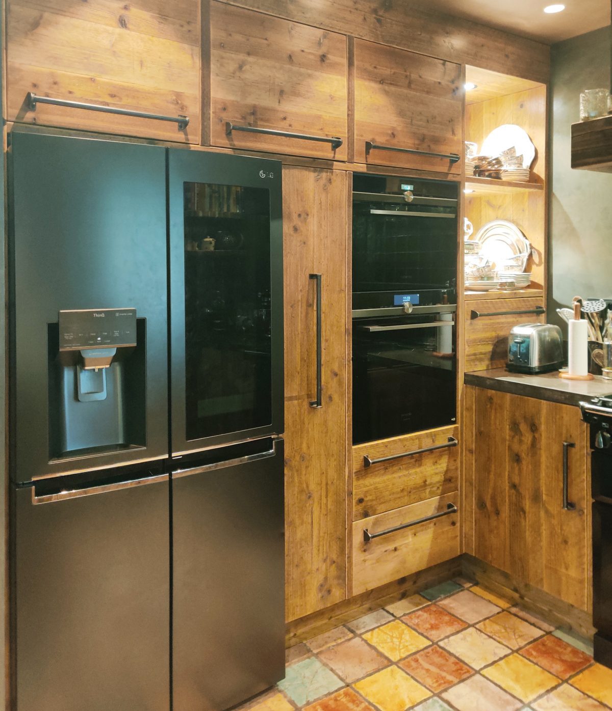 Een grote Amerikaanse koelkast met watertank in een sfeervolle ronde keuken gemaakt van solide steigerhout met op maat gemaakte industriële grepen. Het aanrechtblad en de gootsteen zijn van hardsteen, oftewel natuursteen.